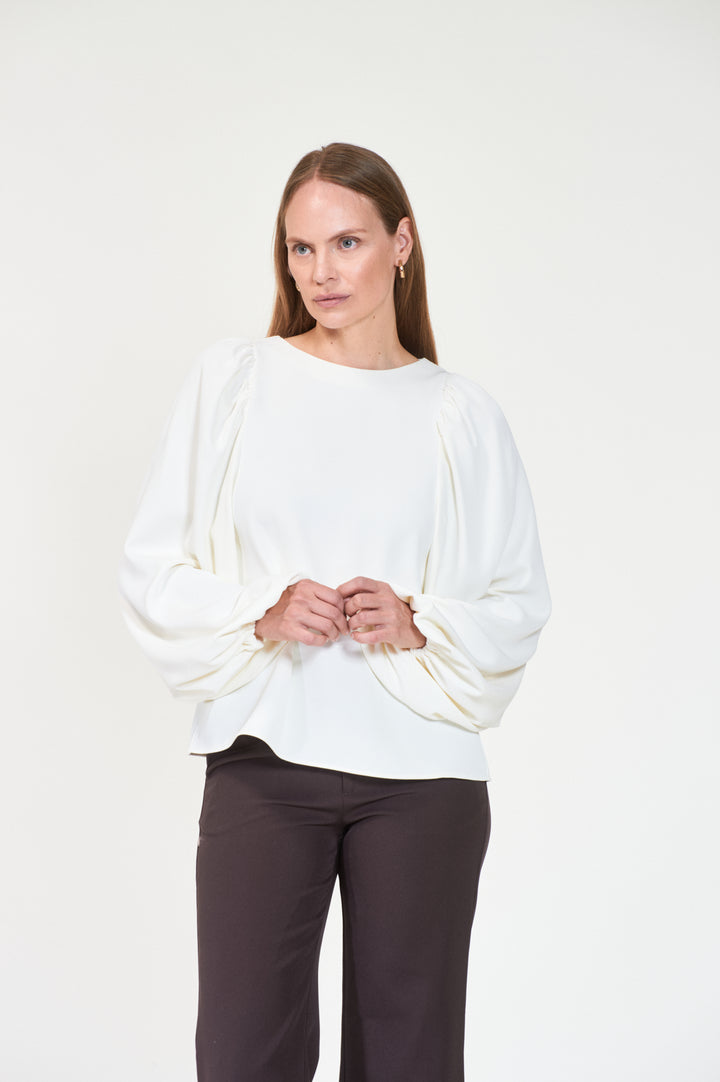 Kremhvit bluse med ballongermer og rund hals, frontsett på modell med mørke bukser