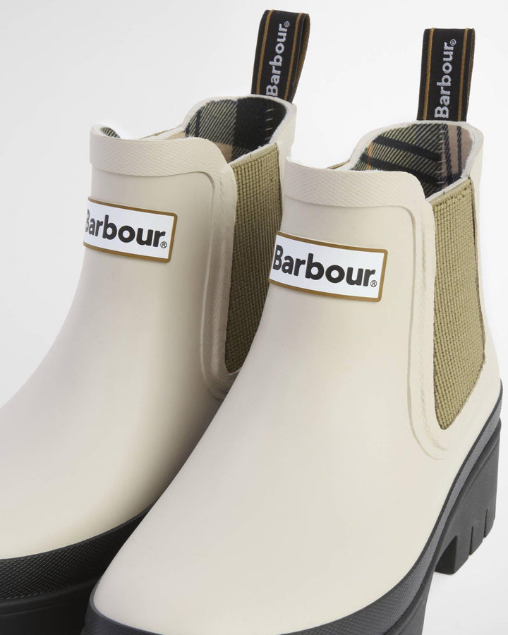 Nært detaljbilde av hælparti med Barbour-logo og olivengrønn elastikk på lyse gummistøvler