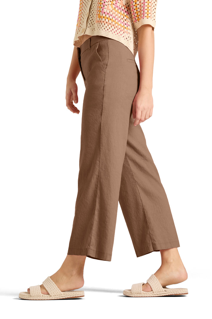 Sidevinkel av beige bukser med vid benkutt og skrålommer, på modell med sandaler
