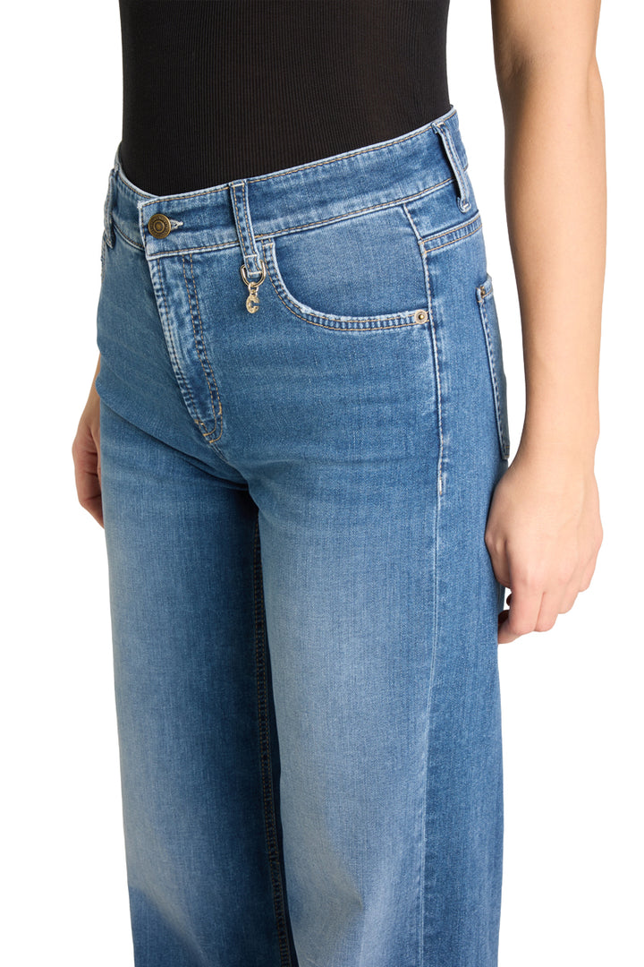 Nærbilde av høy linning med metallknapp, lommekjede og kontrastsøm på medium blå jeans