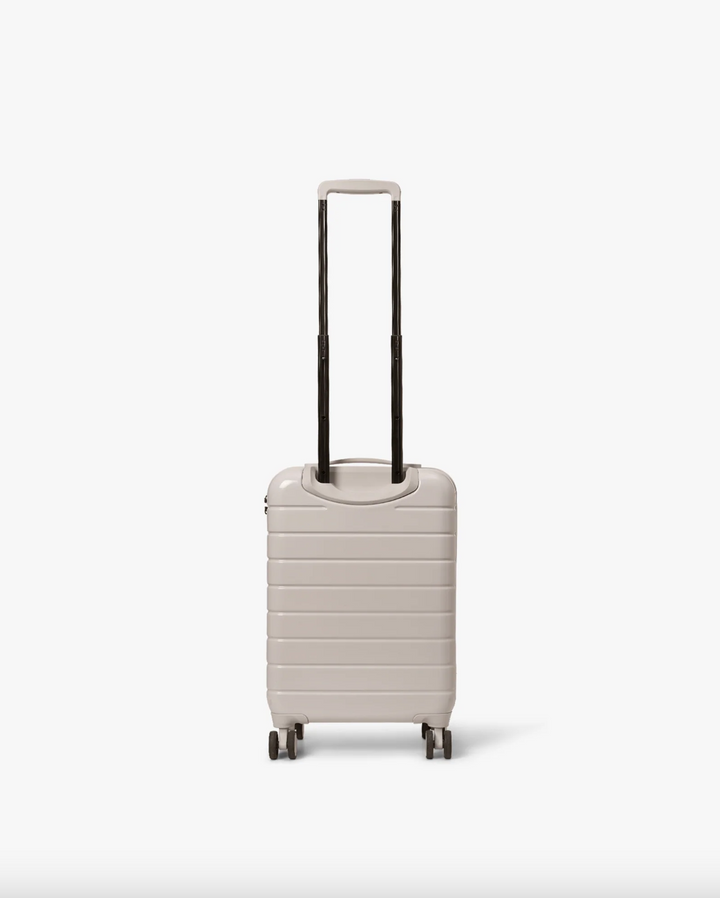 Pastel beige hardskall kabinkoffert med uttrukket teleskophåndtak, bakside med fire hjul synlig