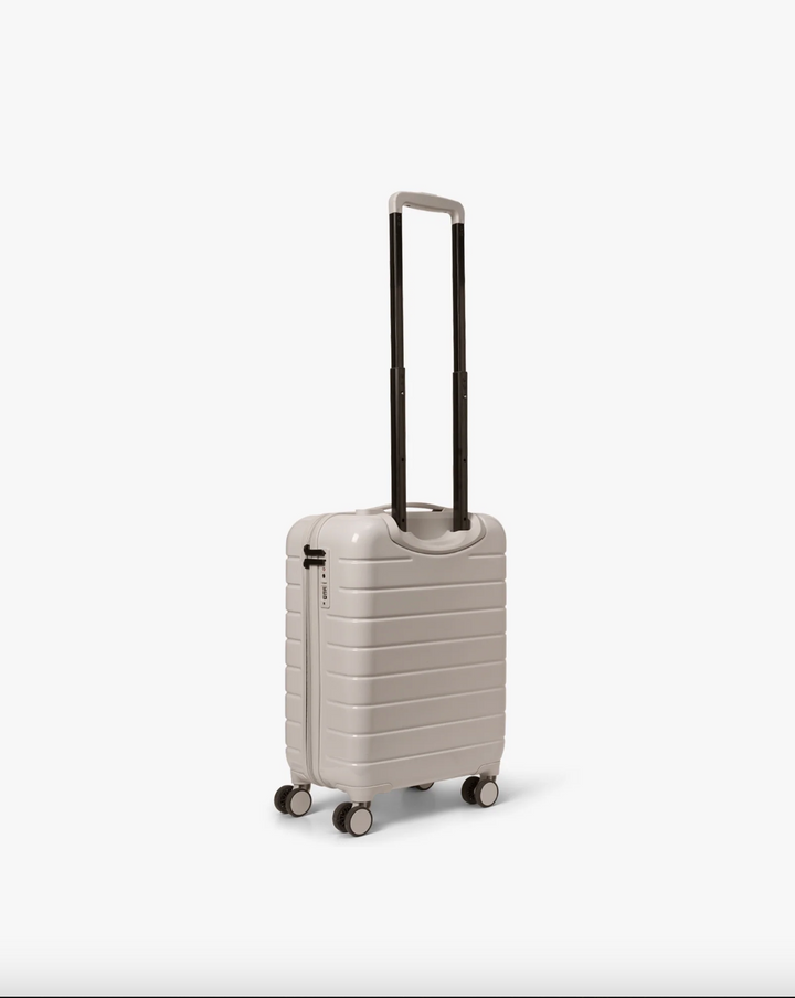 Pastel beige hardskall kabinkoffert med teleskophåndtak utstrakt, sidevinkel med fire hjul synlig