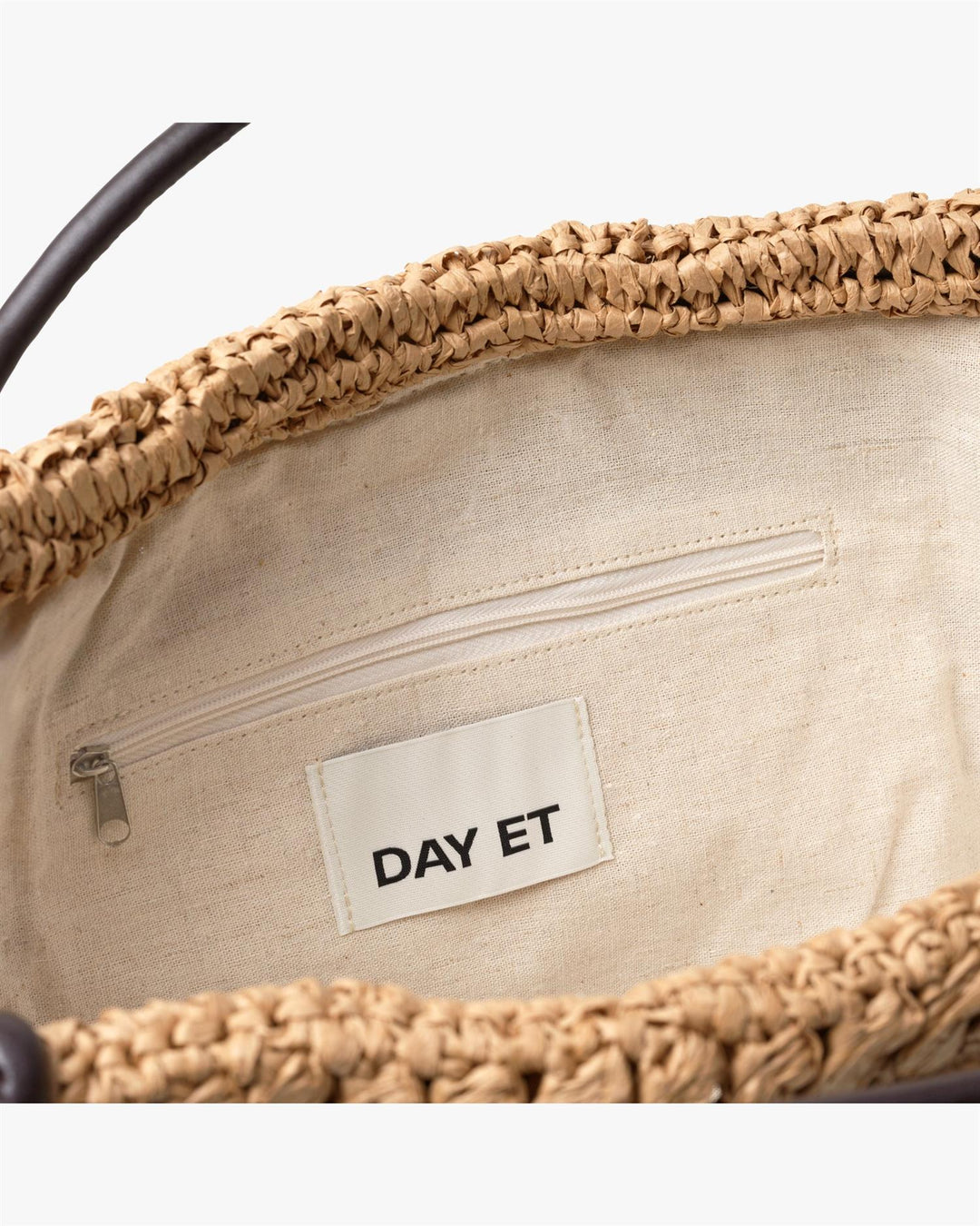 Innsiden av beige strå-veske med lys canvas-fôr, glidelås-lomme og DAY ET-merke synlig