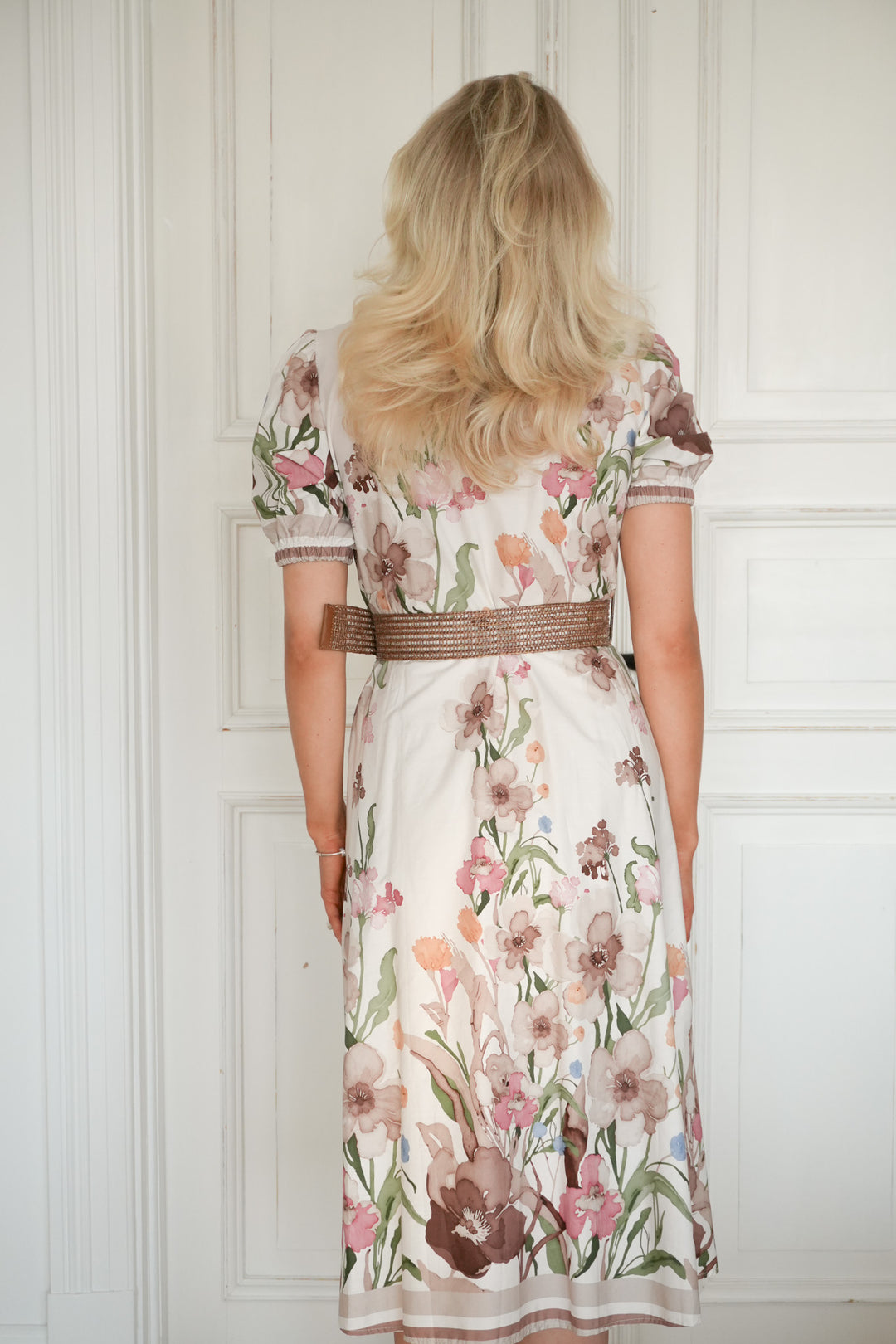 Bakside av blomstret midi-kjole med belte i taljen, vist på modell mot hvit dør