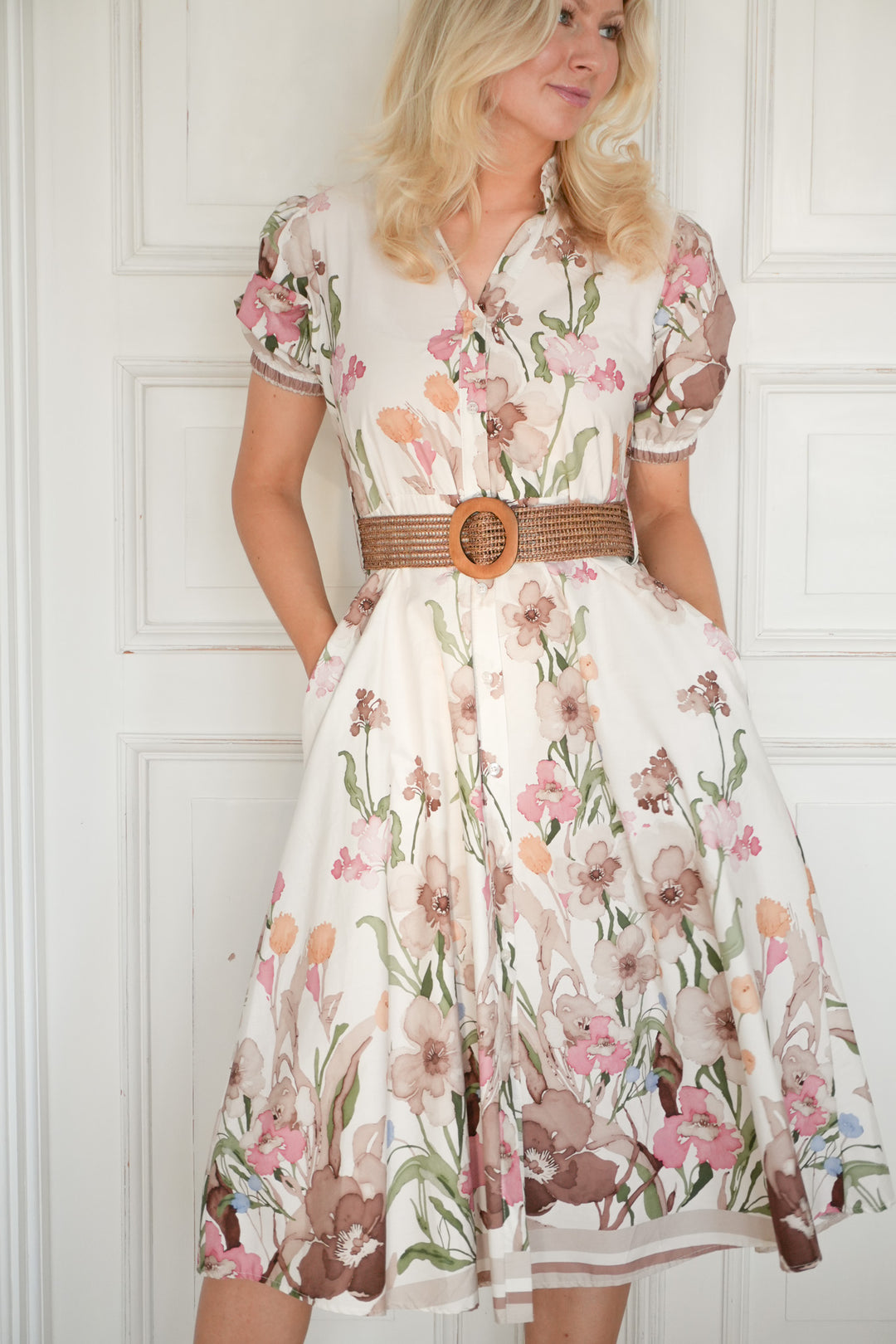 Blomstret kjole med belte, frontsett på modell i helfigur mot hvit vegg