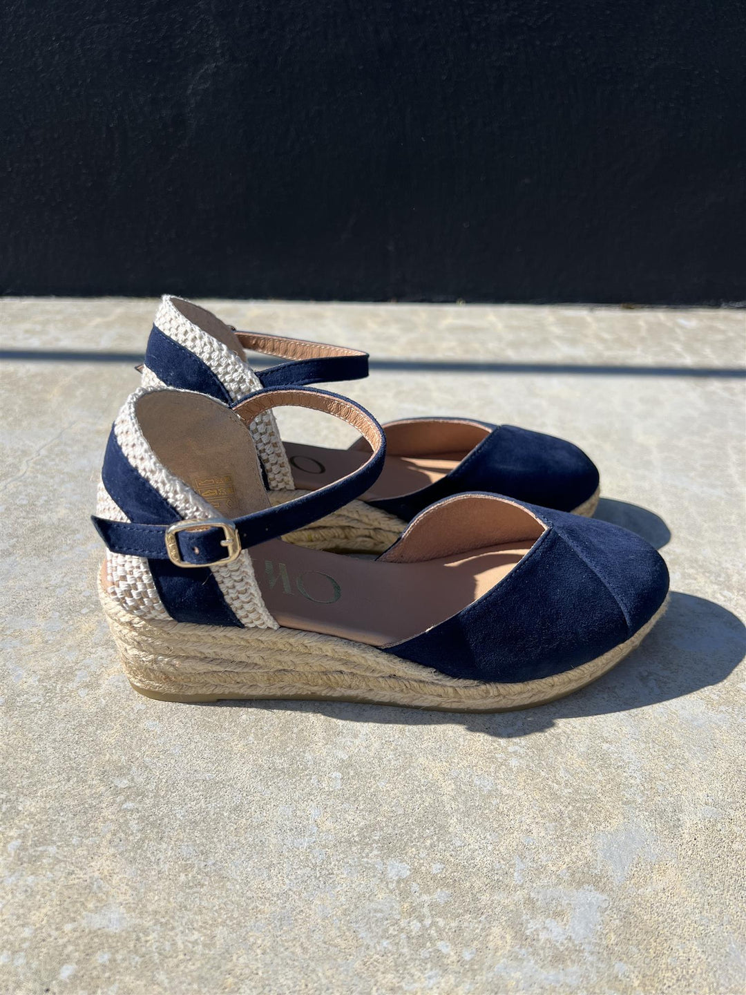 Marineblå espadrille kilehæl sandaler med jute såle, sidevinkel på solbelyst steinflate