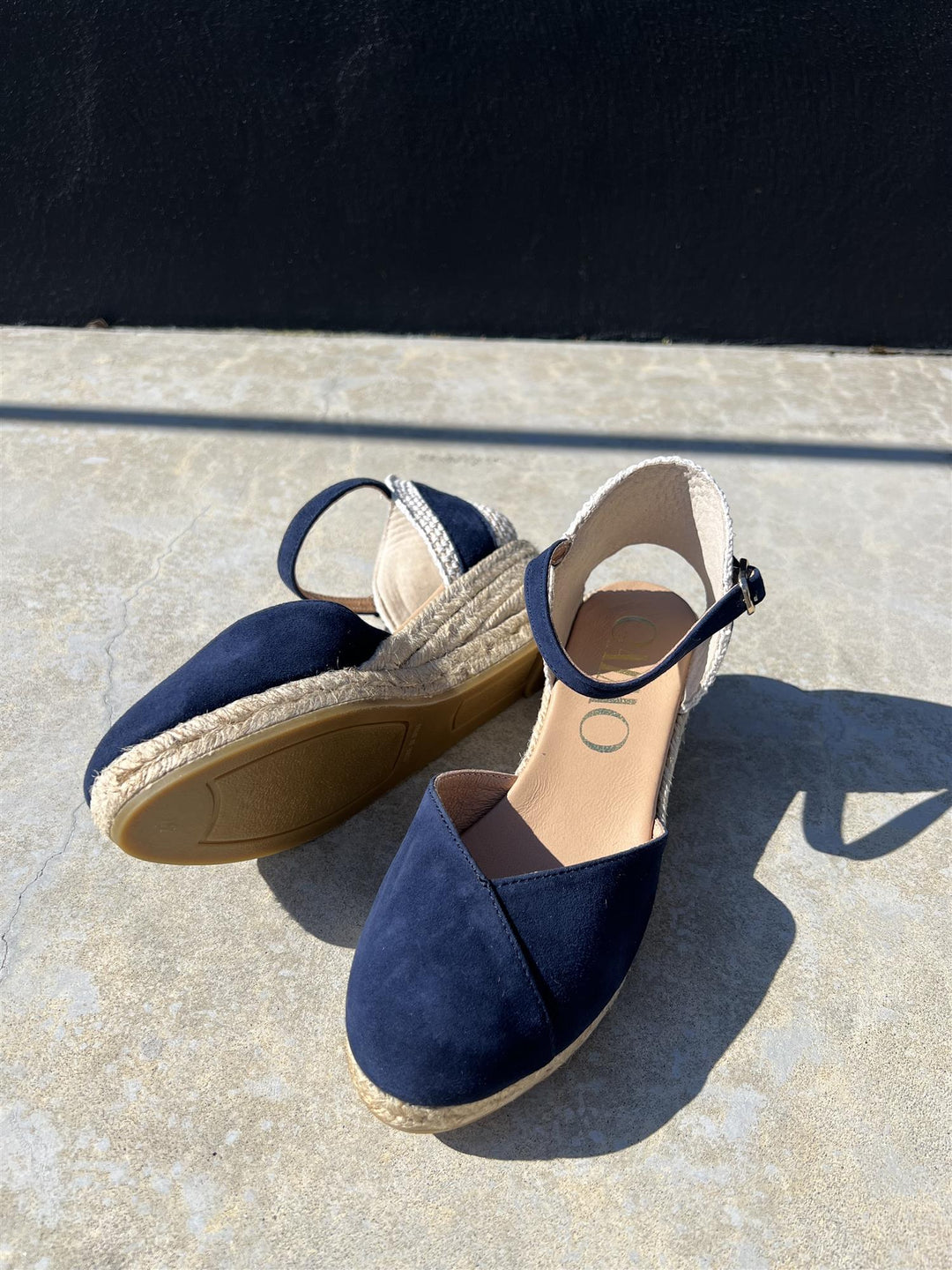 Marineblå espadrille kilehæl sandaler med jute såle, sett ovenfra på lys steinflate i sollys
