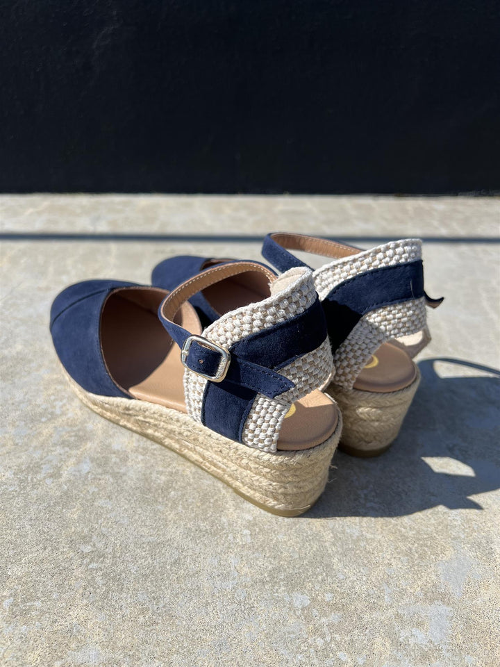 Bakside av marineblå espadrille kilehæl sandaler med jute såle og ankelrem på betongunderlag