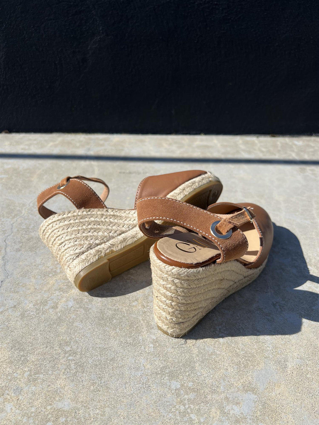 Bakside av brune espadrille kilehæl sandaler med jutefletting og ankelrem på betongunderlag