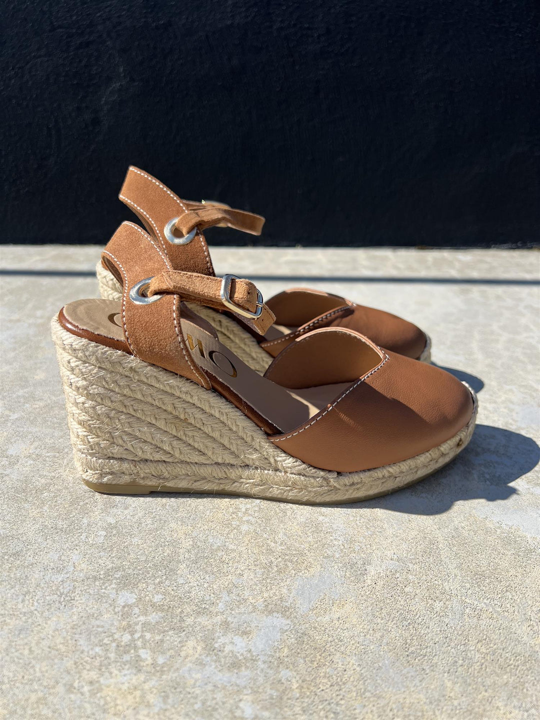 Brune espadrille kilehæl sandaler med jute-såle, sidevinkel på steinflate i sollys