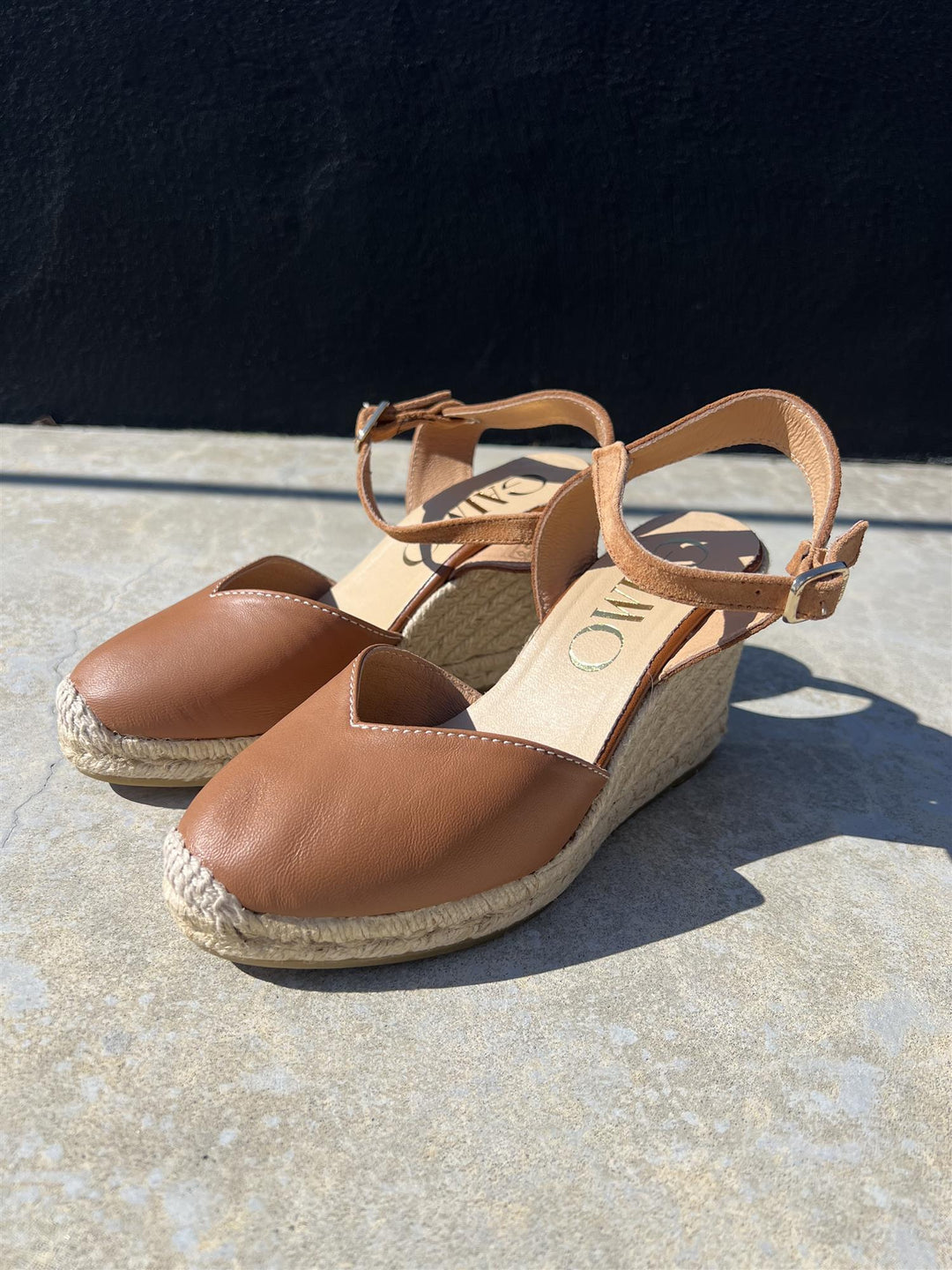 Brune espadrille kilehæl sandaler med ankelrem og jute såle, sidevinkel på betonggulv i sollys