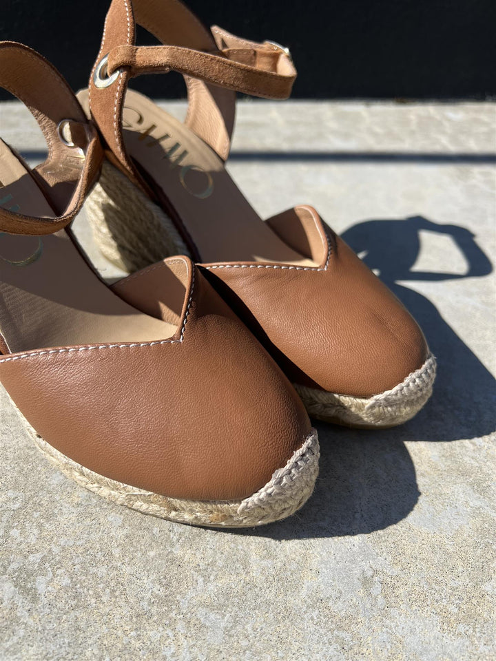 Brune espadrille kilehæl sandaler med ankelrem, frontsett på solbelyst steinflate med skygge