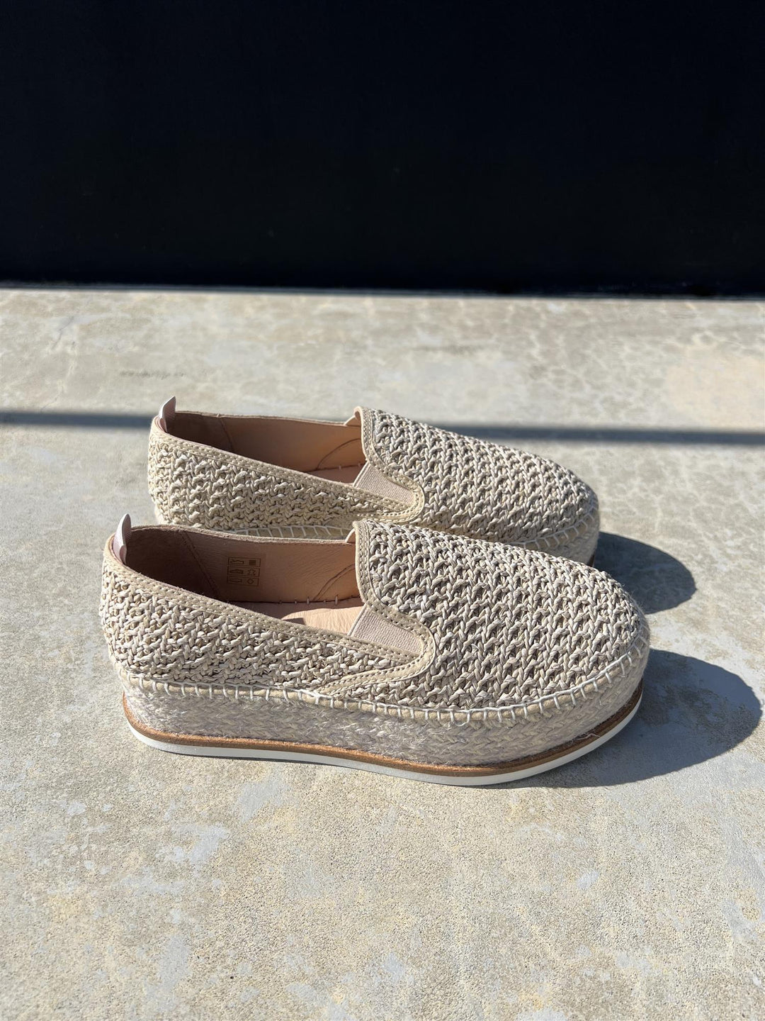 Sidevinkel av heklede espadrillesko i sahara med platåsåle og jutefletting på steinfliser