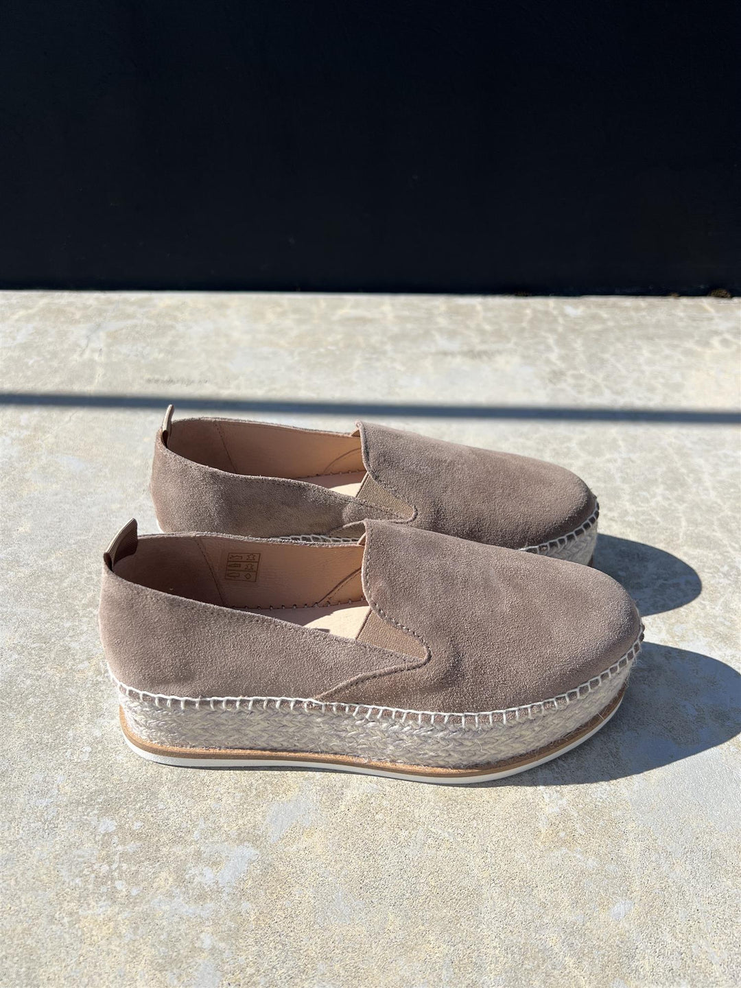 Taupe espadrilles med jute-såle og hvit gummibunn, sidevinkel på steinfliser i sollys
