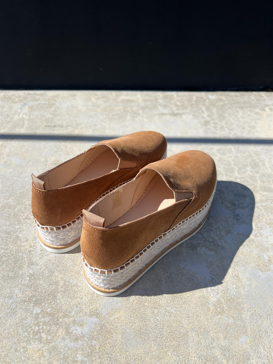 Brune espadrille-sko med jute-såle og hvit gummibunnen, bakside-vinkel på steinfliser i sollys