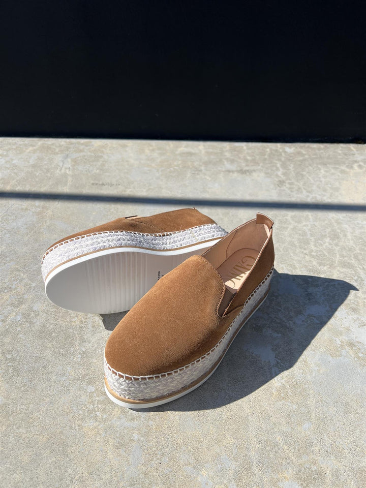 Brune espadrille-sko i semsket skinn med jute-såle, sidevinkel på steinfliser i sollys