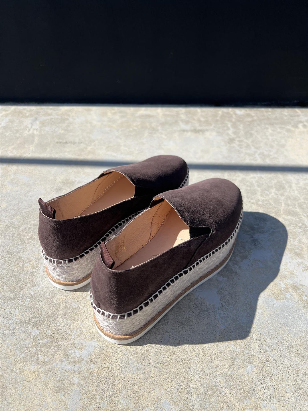 Bakside av chokoladebrun espadrille slip-on sko med jutetau og platåsåle på steinfliser