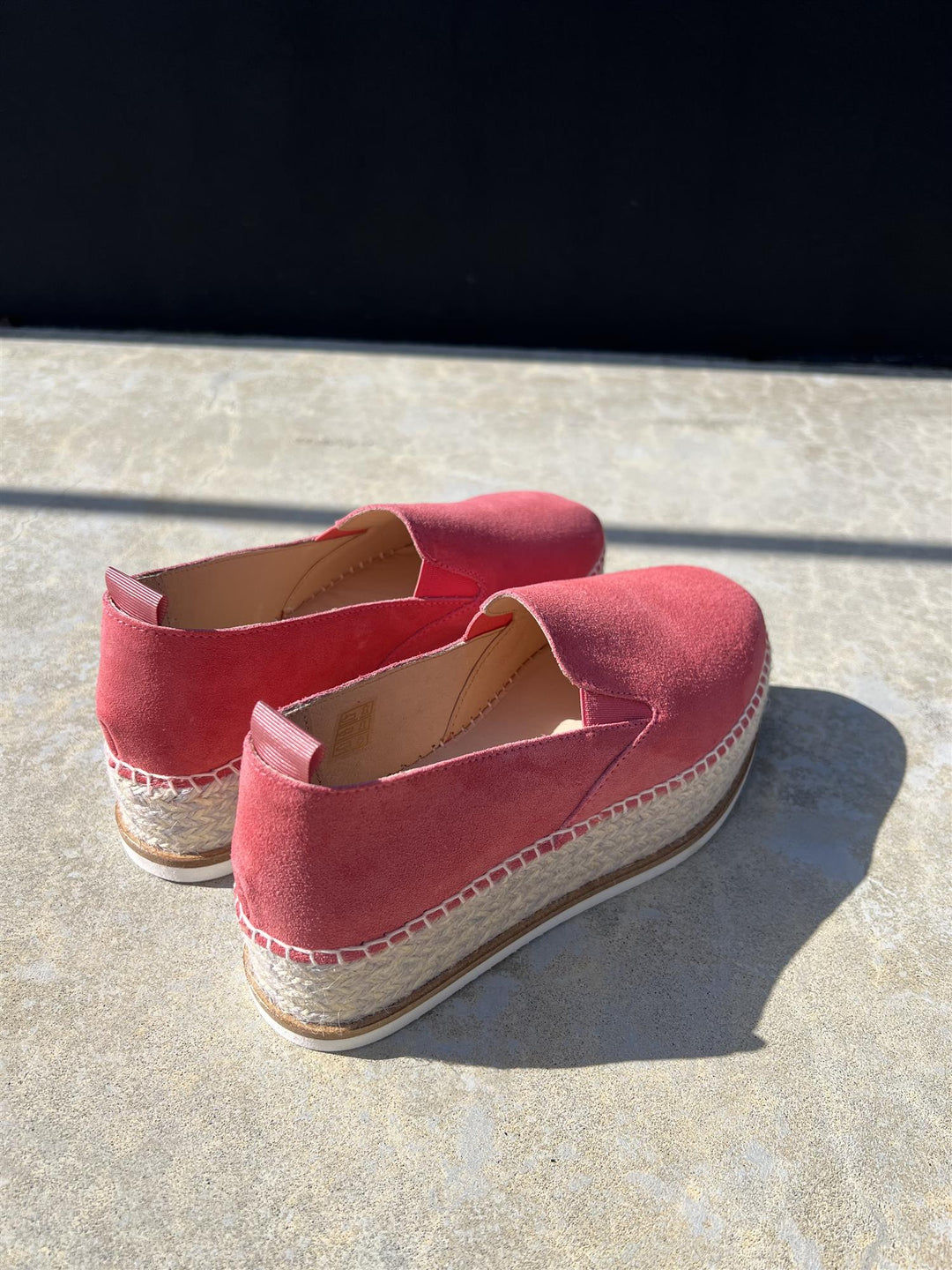 Bakside av korallrosa espadrille slip-on sko med platåsåle og jutefletting, solbelyst på betong