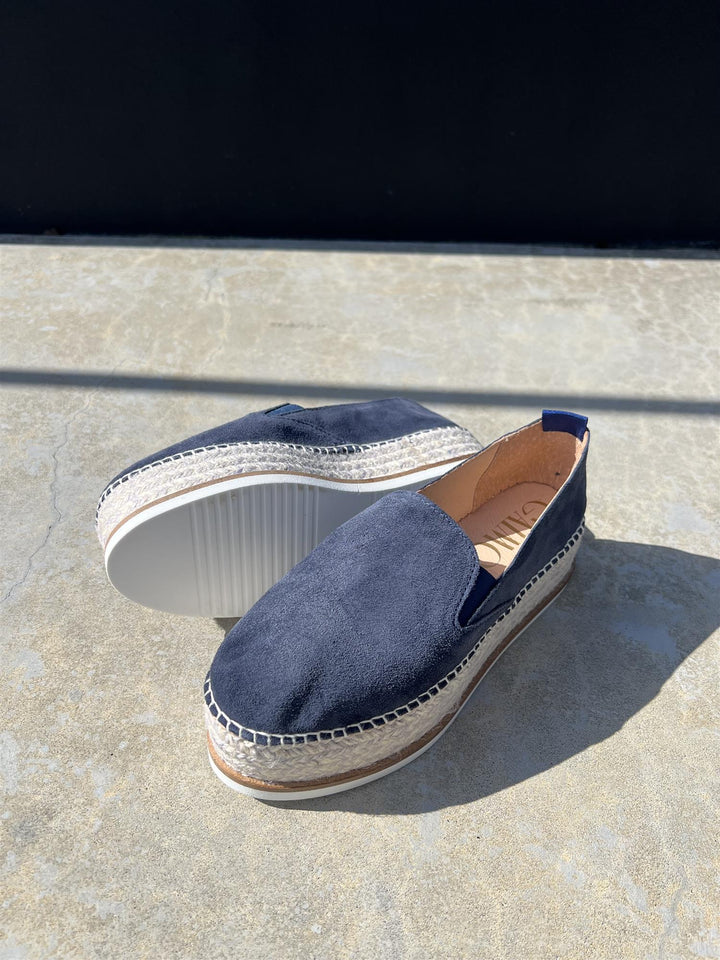 Mørkeblå espadrille slip-on sko med platåsåle og jutefletning, sidevinkel på steinfliser i sollys