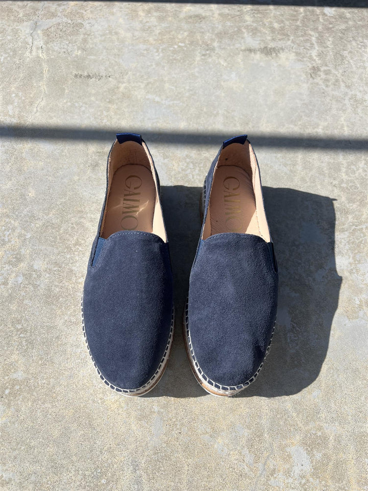 Mørkeblå espadrille slip-on sko med juteflettet platåsåle, ovenfra på steinfliser i sollys