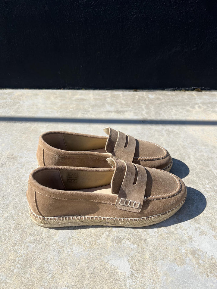 Beige semsket loafers med espadrille-såle og penny loafer-rem, sidevinkel på solbelyst betongunderlag