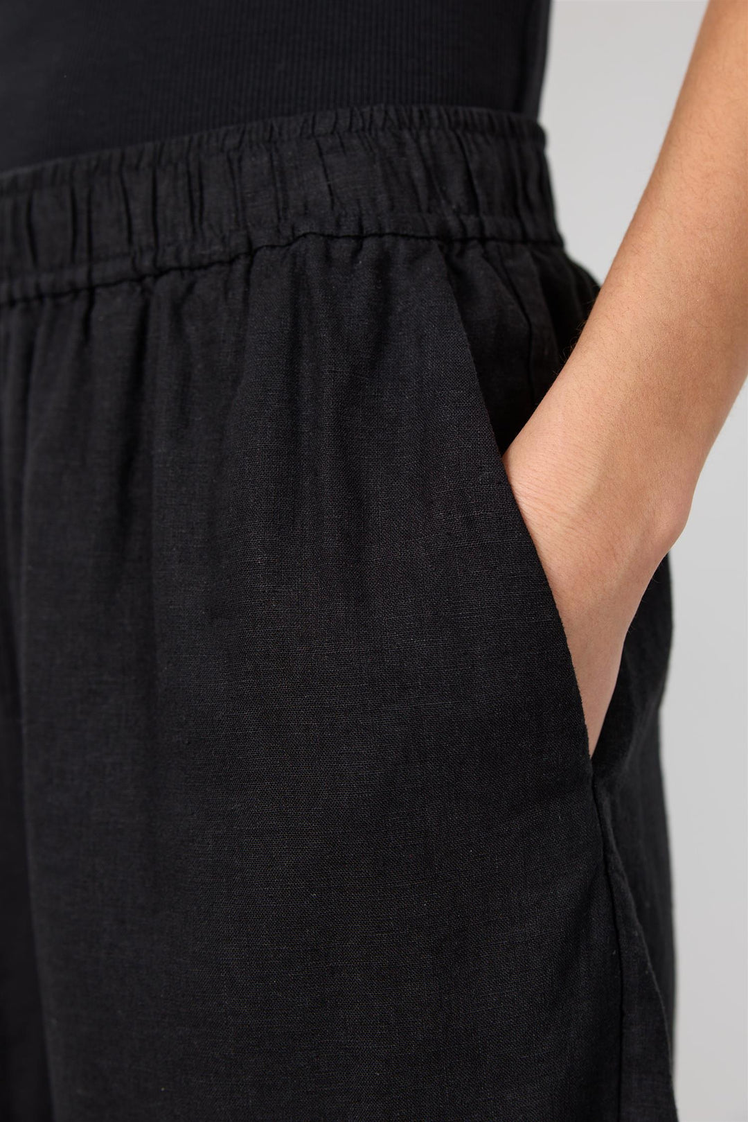 Sidevinkel av svarte shorts med hånd i lomme, viser elastisk linning og avslappet passform