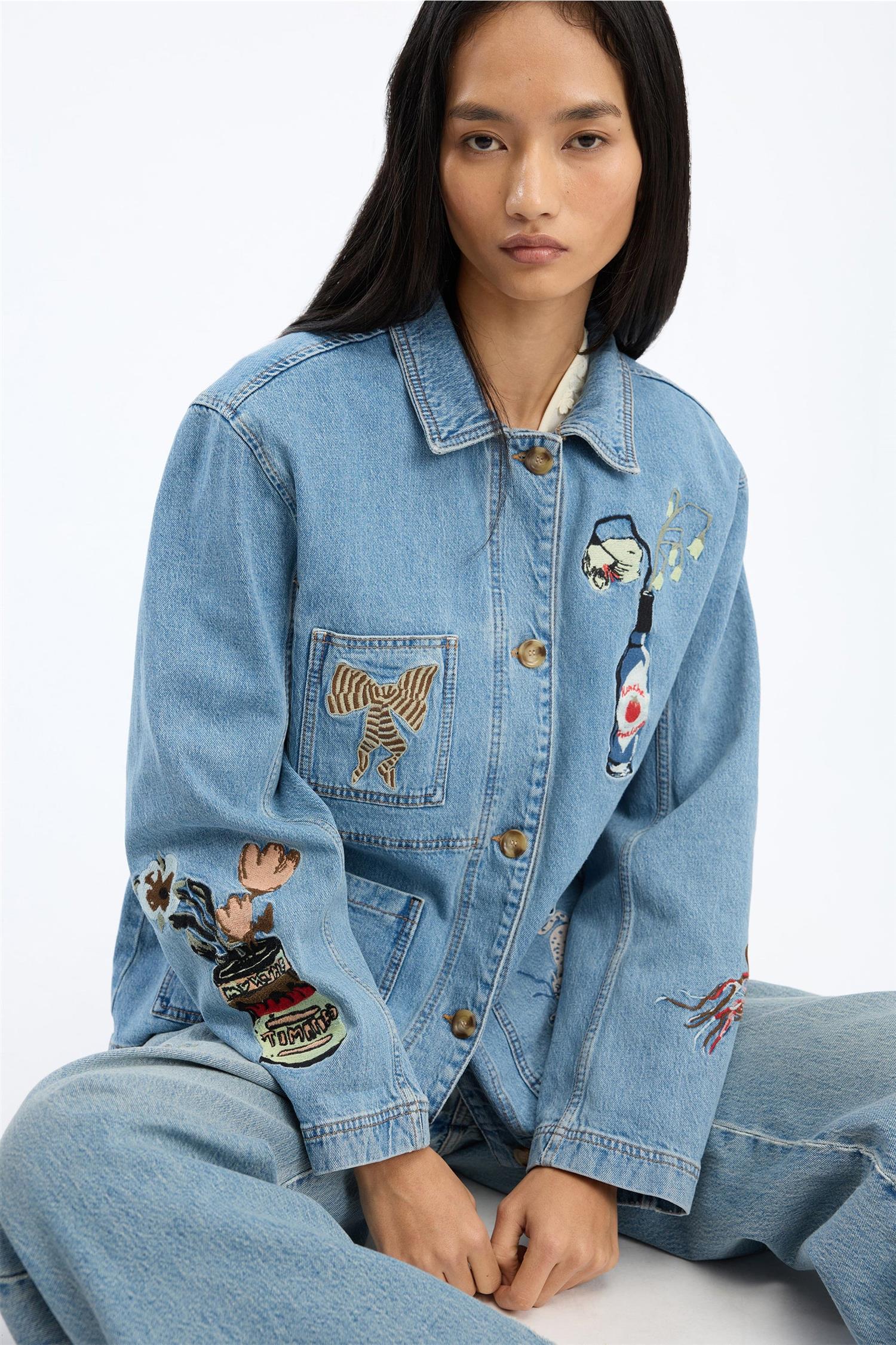 Blå denimjakke med broderte motiver på bryst og ermer, frontsett på sittende modell