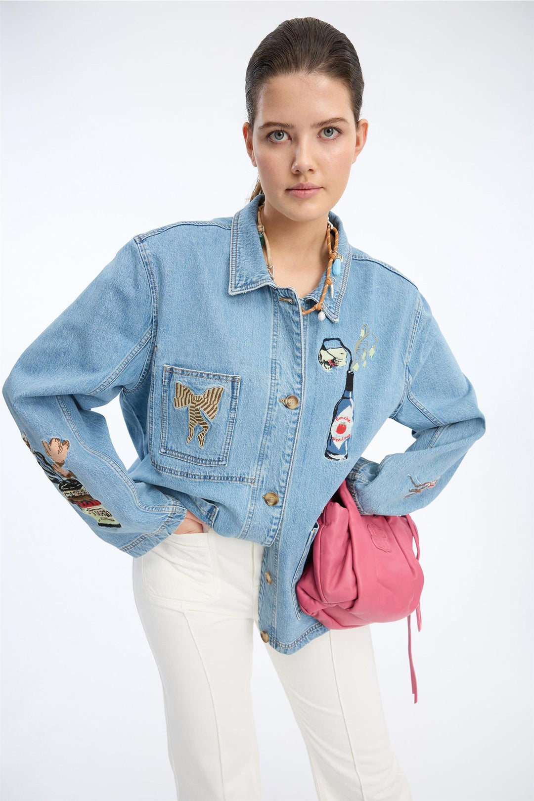 Blå denimjakke med broderte motiver på bryst og ermer, frontsett på modell med rosa veske