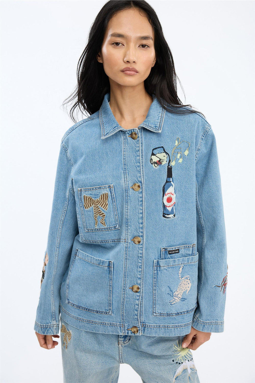Blå denimjakke med broderte motiver og fire frontlommer, frontsett på modell i studio