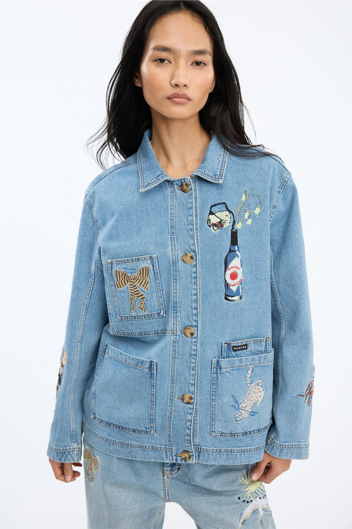 Blå denimjakke med broderte motiver og fire frontlommer, frontsett på modell i studio