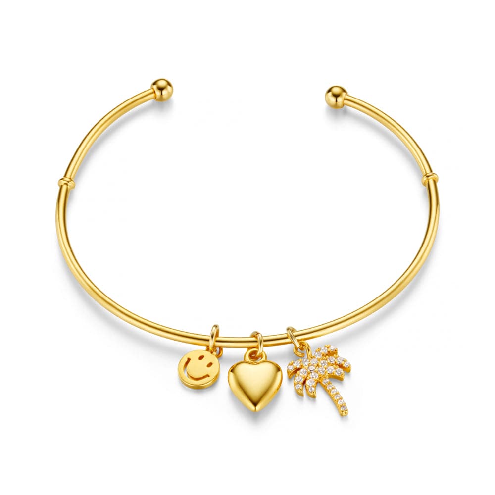 Gullbelagt åpen bangle-armbånd med tre charms: smiley, hjerte og palmetreet, frontsett på hvit bakgrunn