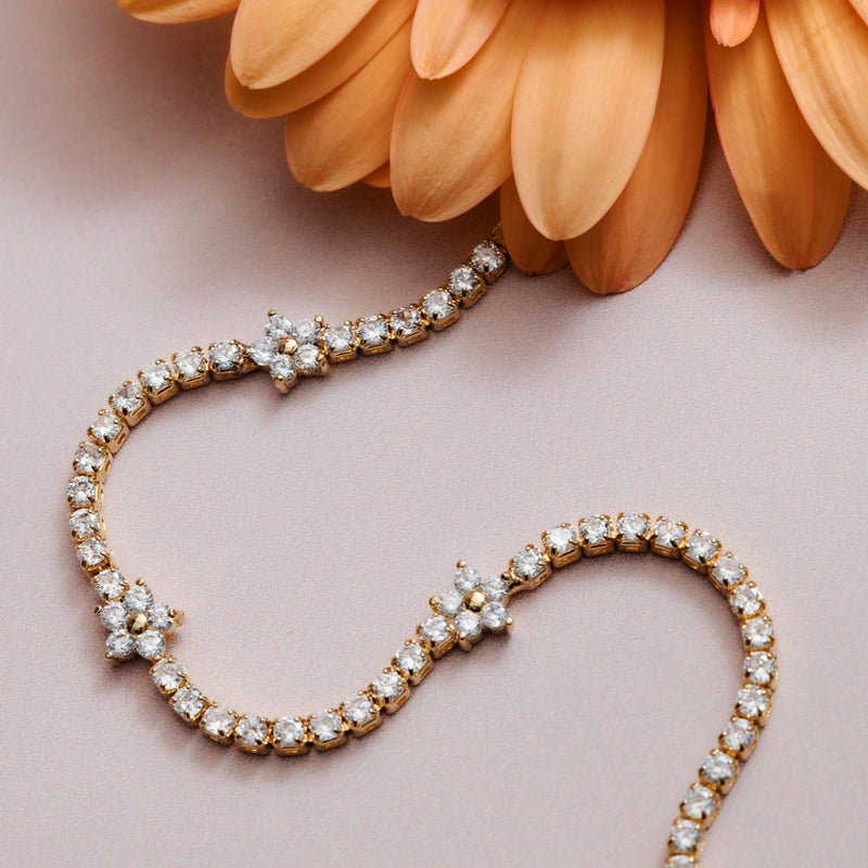 Gulltonet tennis armbånd med cubic zirconia og blomsterdetaljer, flat lay ved orange blomst