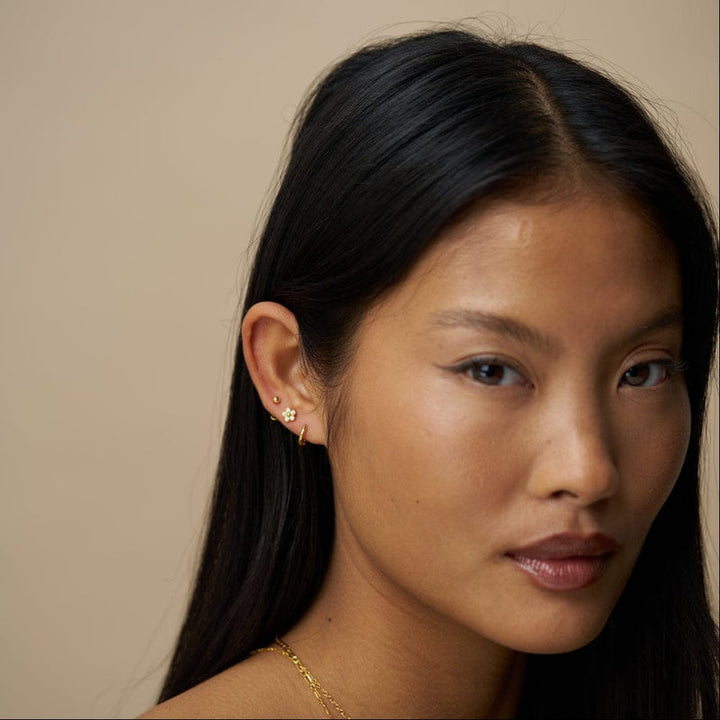 Gullbelagt ørepyntsett med blomster studs, ball studs og micro hoops vist på modells øre