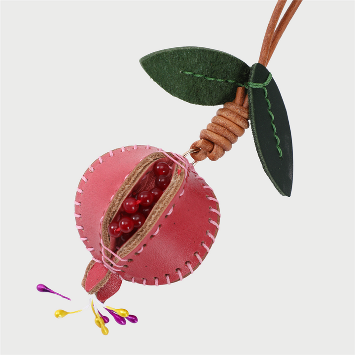 Rosa granateple-charm med åpen design som viser røde perler innvendig, grønne filtblader og lærsnor